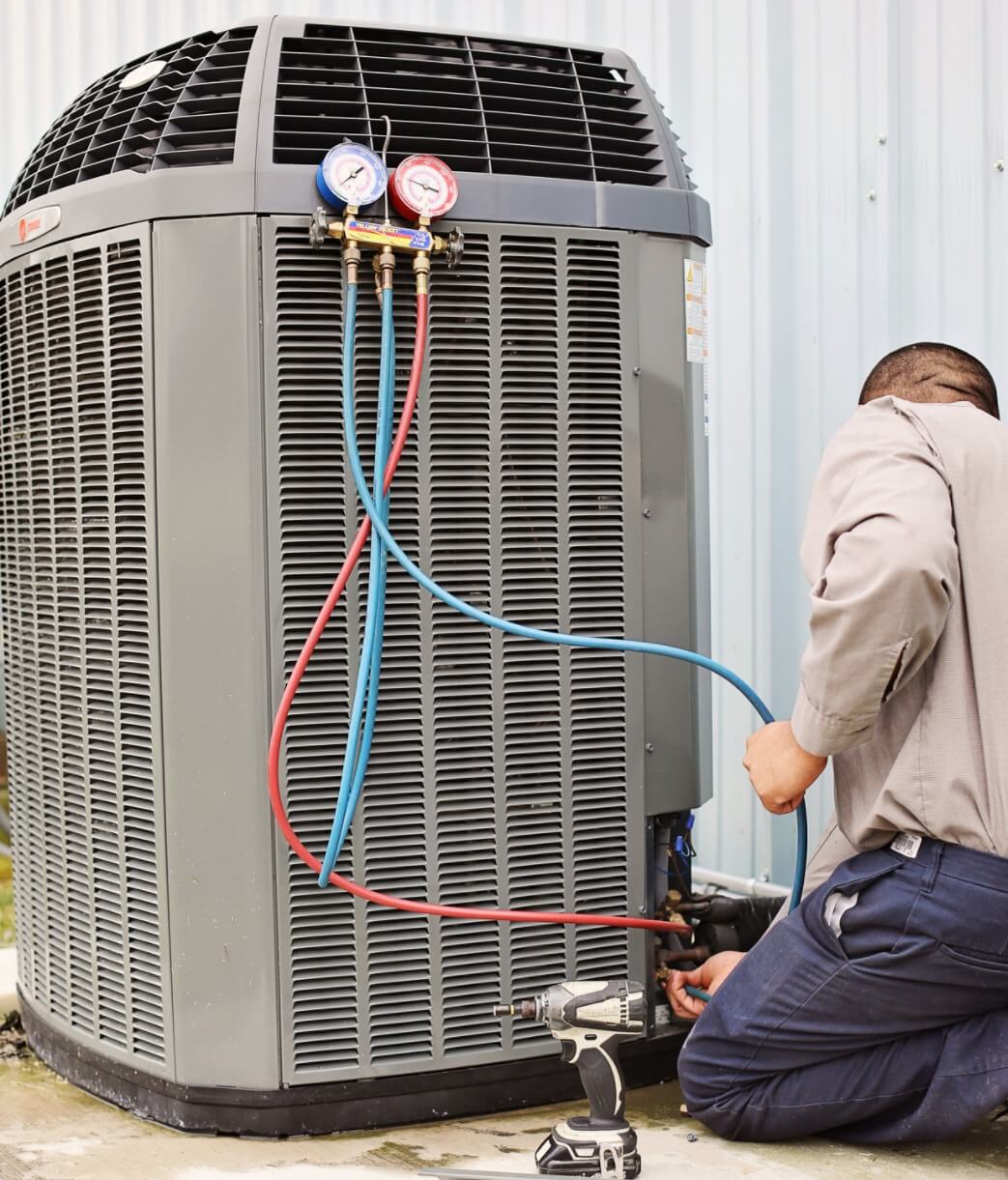 BHMS technician servicing an outdoor heat pump unit with refrigerant gauges