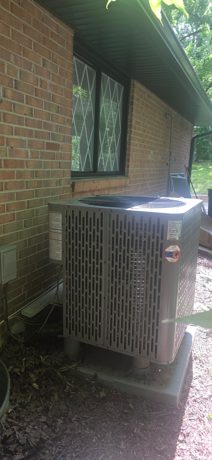 Outdoor AC condenser unit beside a brick home